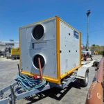 Trailer-mounted Psilos Group rooftop heat pump unit with dual fan grilles, parked outdoors on a paved yard.